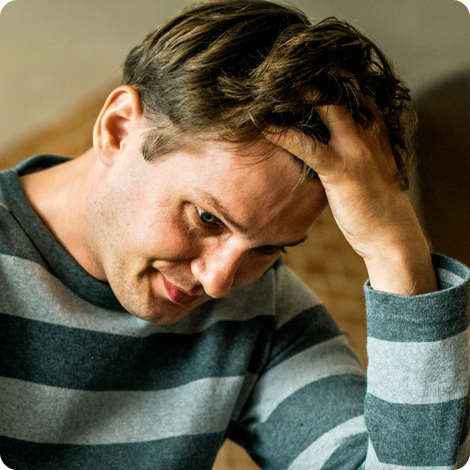 close up image of man in striped shirt running hands through his hair while looking worried