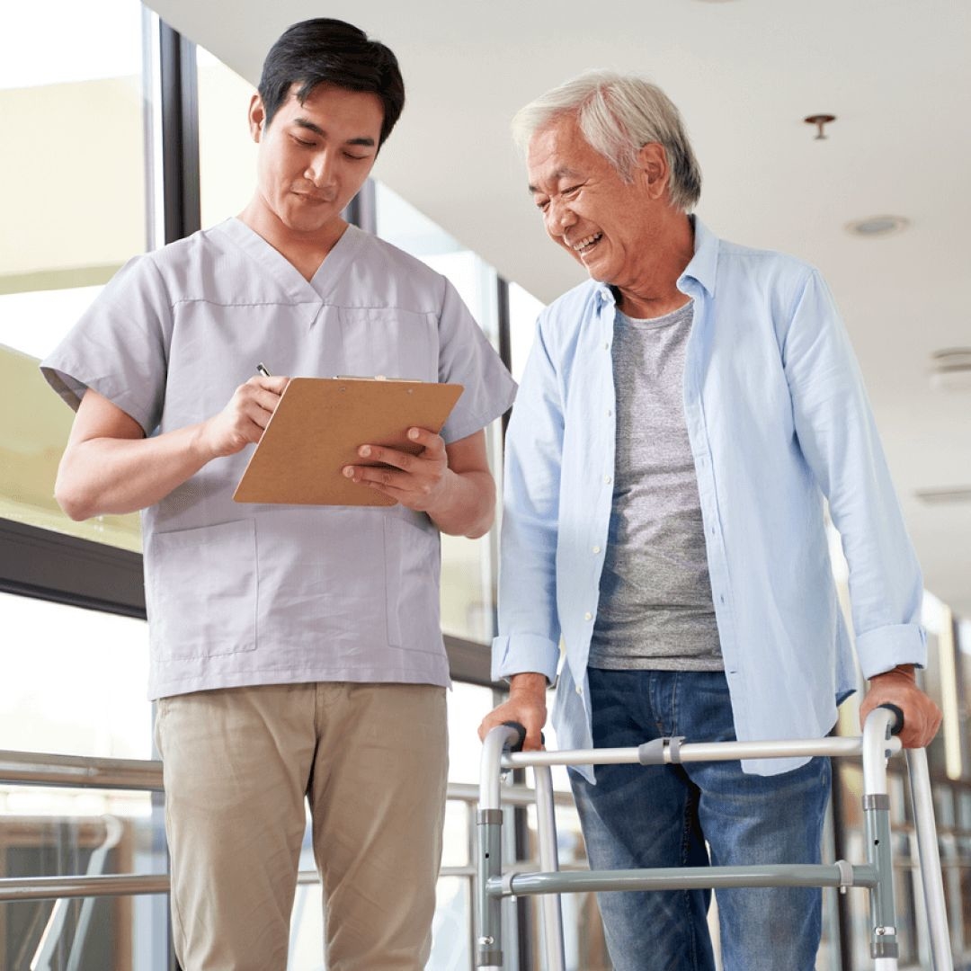 A male physical therapist jots down a SOAP note for physical therapy while treating a male patient.