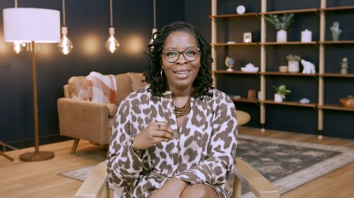 woman with glasses and smiling, sitting in a chair for an interview