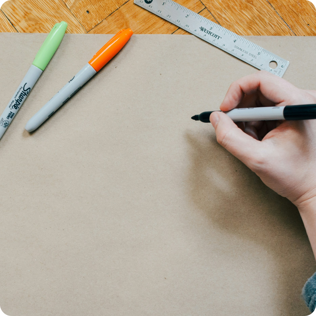 close up of person's hand drawing on paper with markers and a ruler