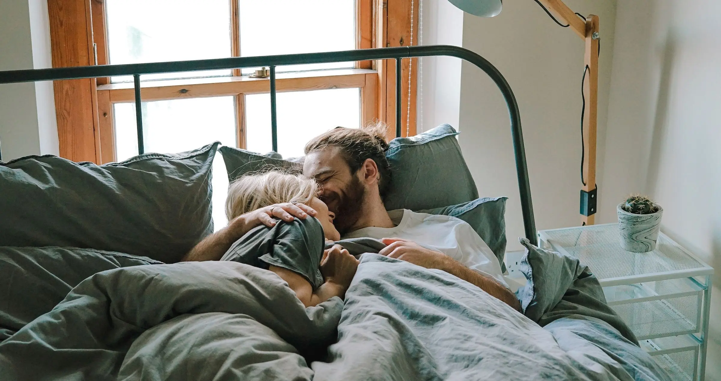Everyman - Glückliches, lächelndes Paar liegt Arm in Arm im Bett und kuschelt