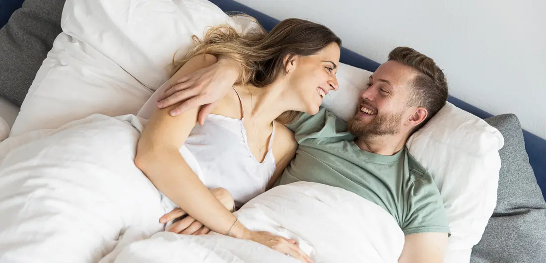 Everyman - Glückliches, lächelndes Paar liegt Arm in Arm im Bett und kuschelt