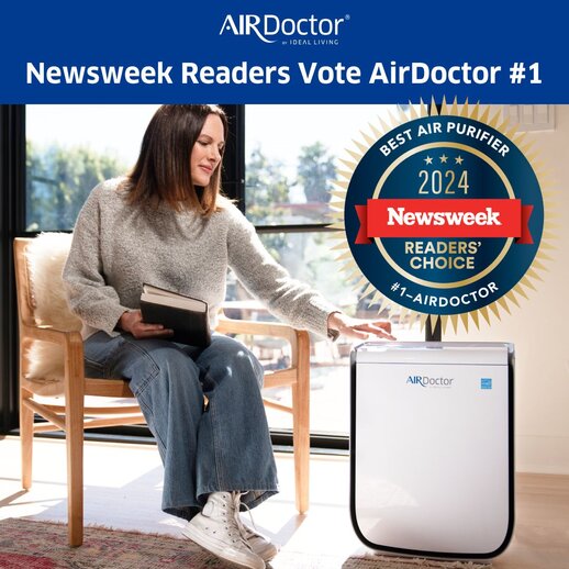 A woman sits on a chair next to an AirDoctor purifier, holding a book, with a Newsweek award badge