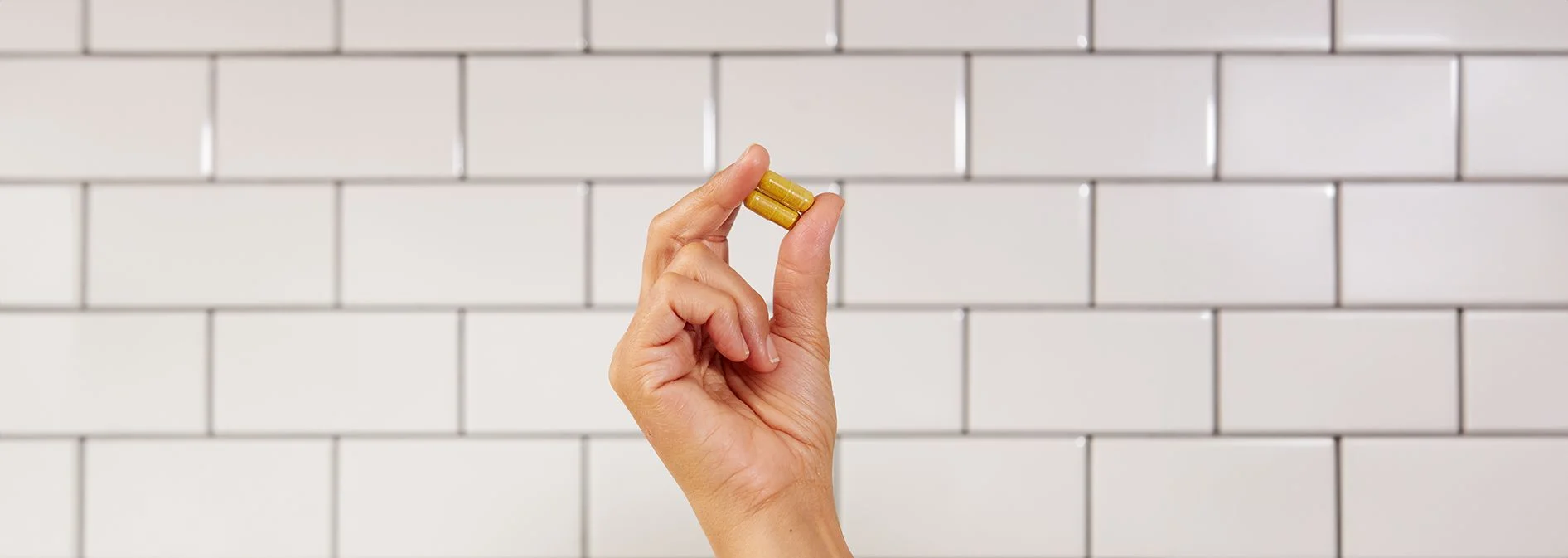 A hand holding two capsules of NativePath Naive Berberine with white subway tile in the background. 