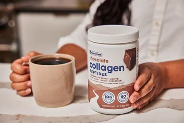 A woman pouring a scoop of NativePath Chocolate Collagen into a glass of almond milk