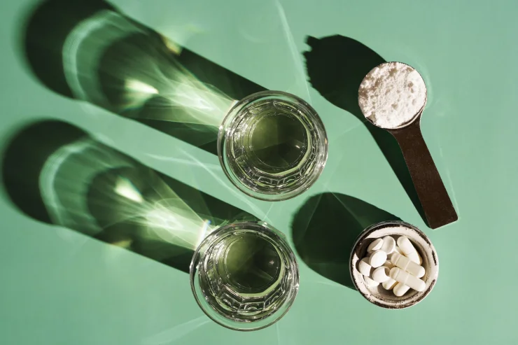 A scoop of grass-fed collagen powder and probiotic capsules alongside two clear glasses of water. Top-view.