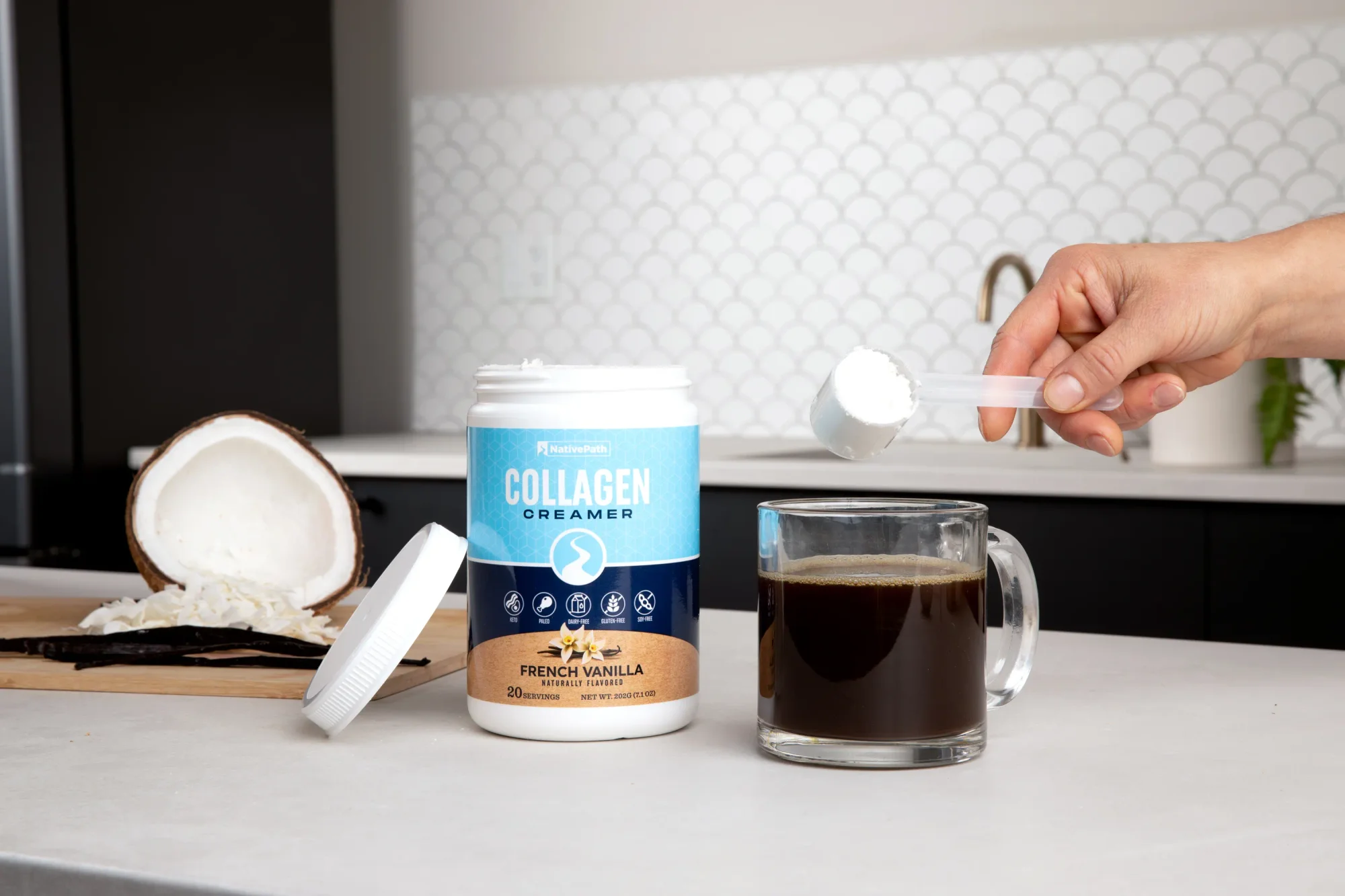 Hand putting a scoop of NativePath Collagen Creamer into a clear cup of black coffee. Kitchen setting.