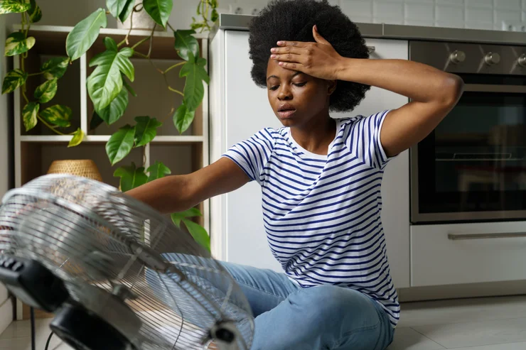 A woman sitting on the floor with a fan experiencing a hot flash