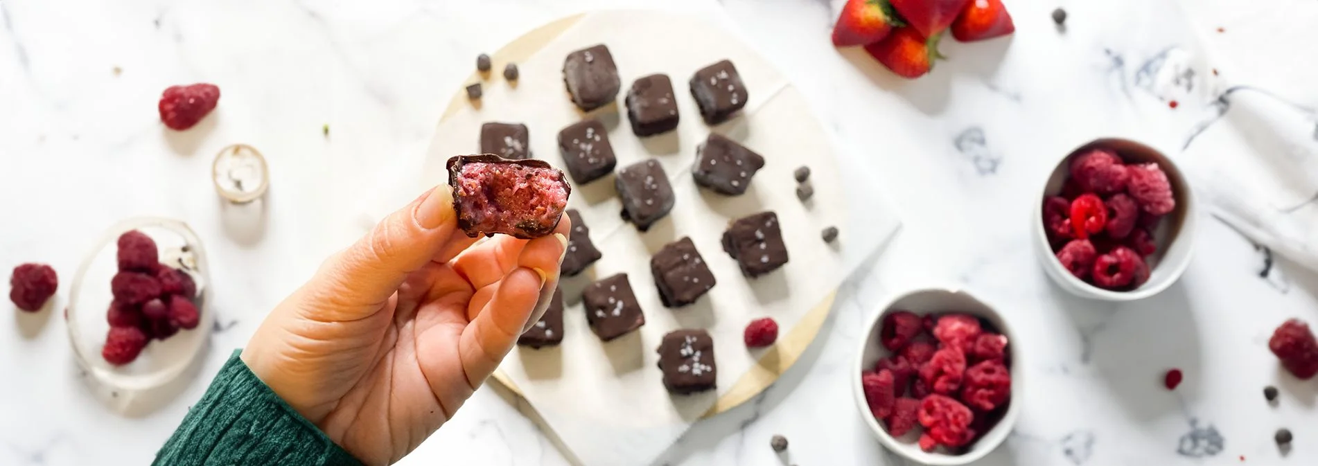 A hand holding a chocolate berry bites with more in the background