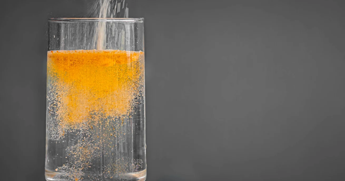 A glass of water with an orange NAC powder being mixed into it