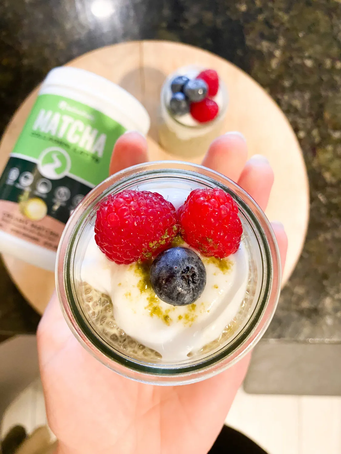 Woman holding a clear jar of Matcha Collagen Chia Seed Pudding, topped with fresh raspberries and blueberries. NativePath Matcha Collage jar in background.