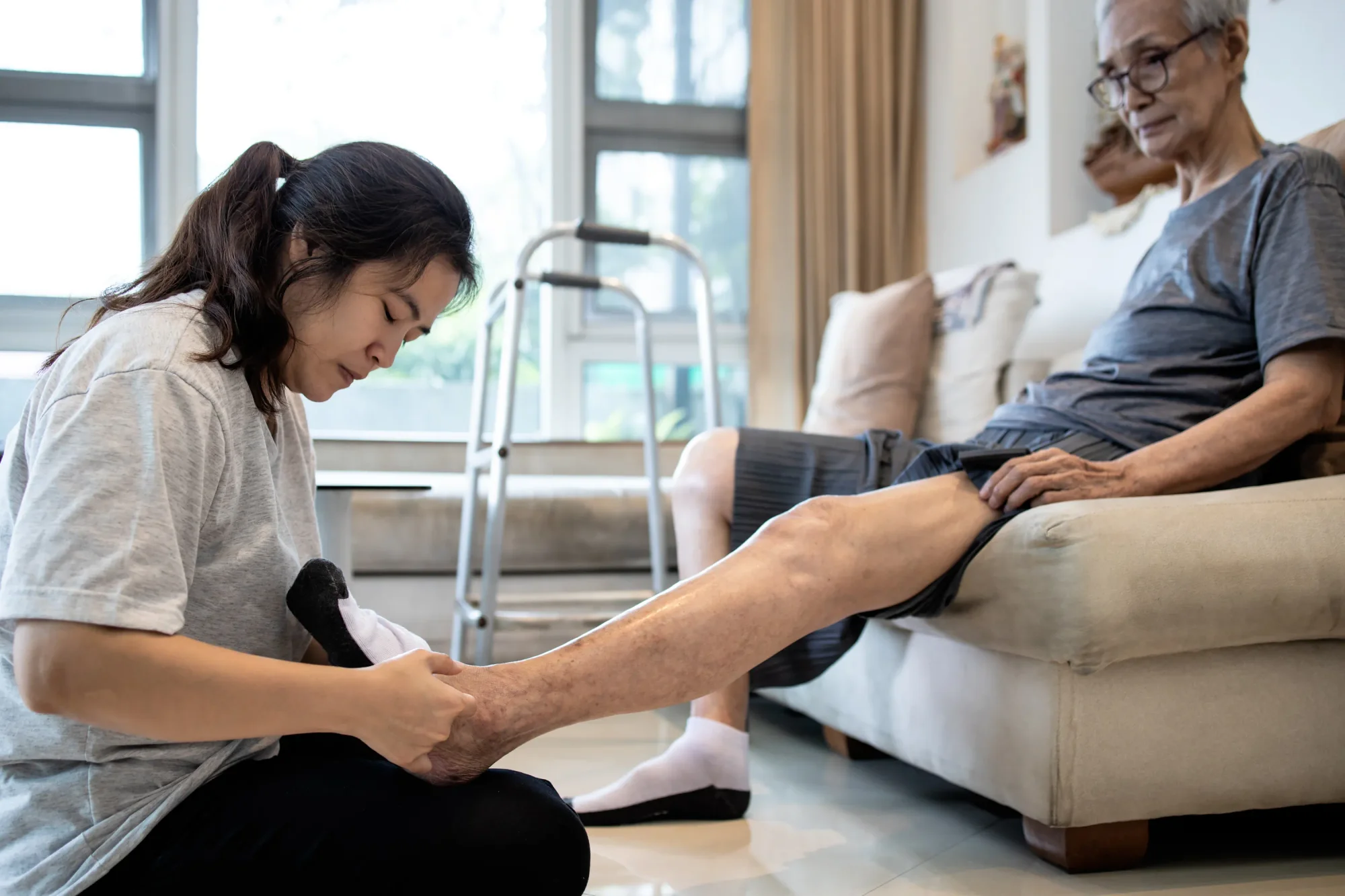 Asian daughter helping elderly dad put on socks for neuropathy.