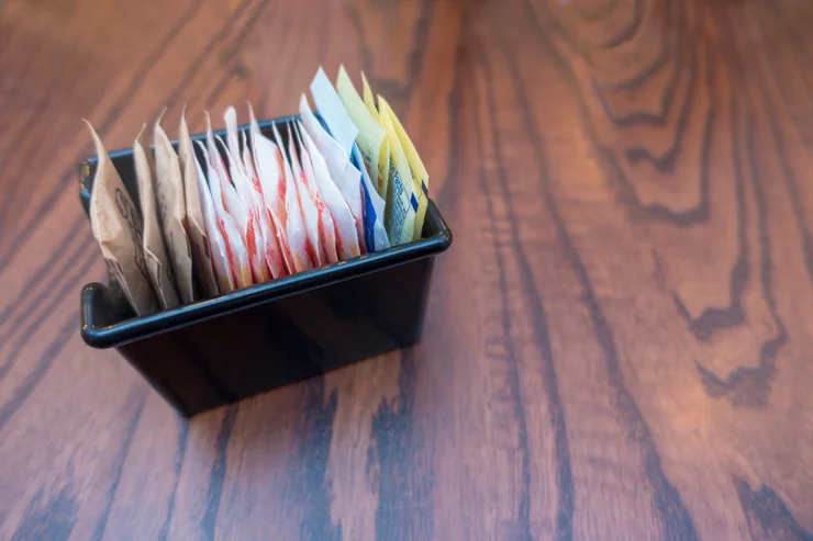 A container holding packets of several different artificial sweetener packets