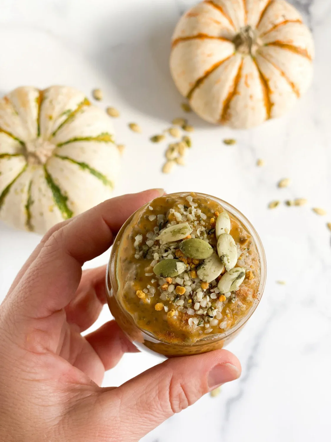 Hand holding pumpkin chia seed pudding with pumpkins in the background