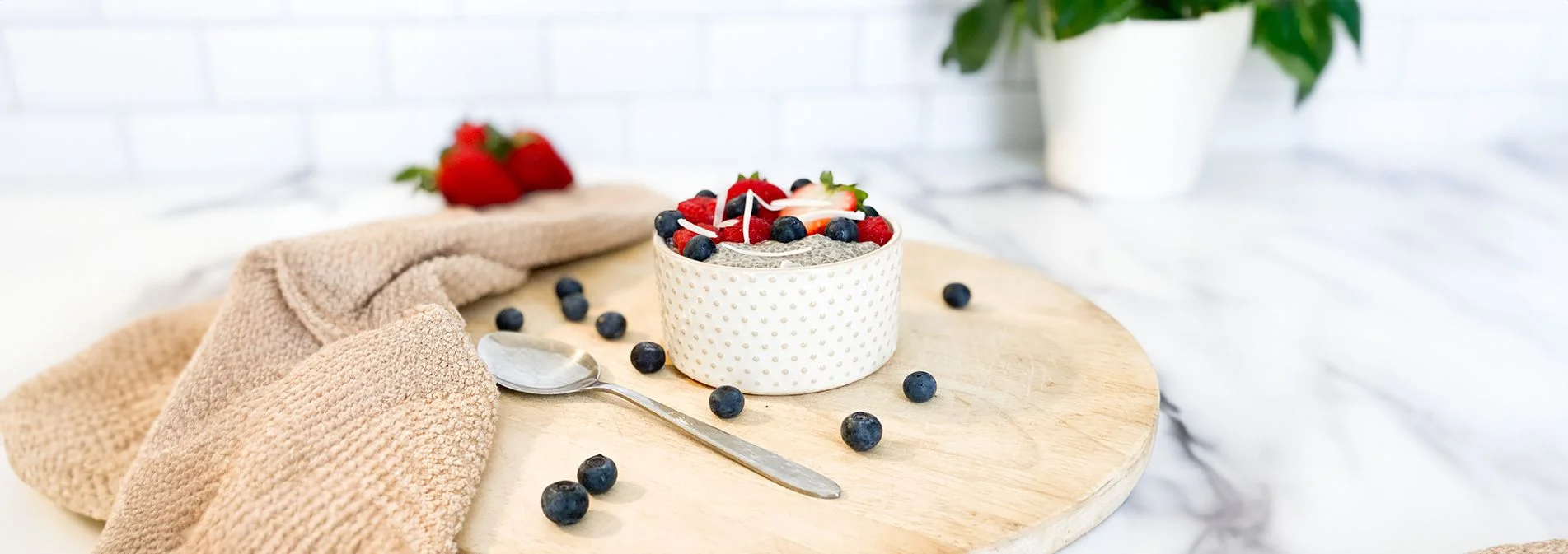 Ceramic bowl of vanilla chia pudding with fresh berries sprinkled on top. Silver spoon laying next to bowl.