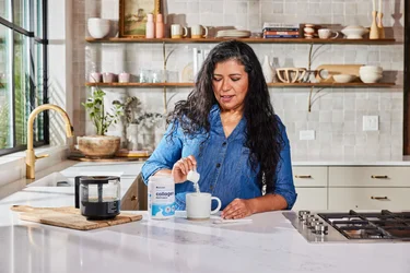 A woman pouring a scoop of NativePath original collagen pepides into a coffee mug