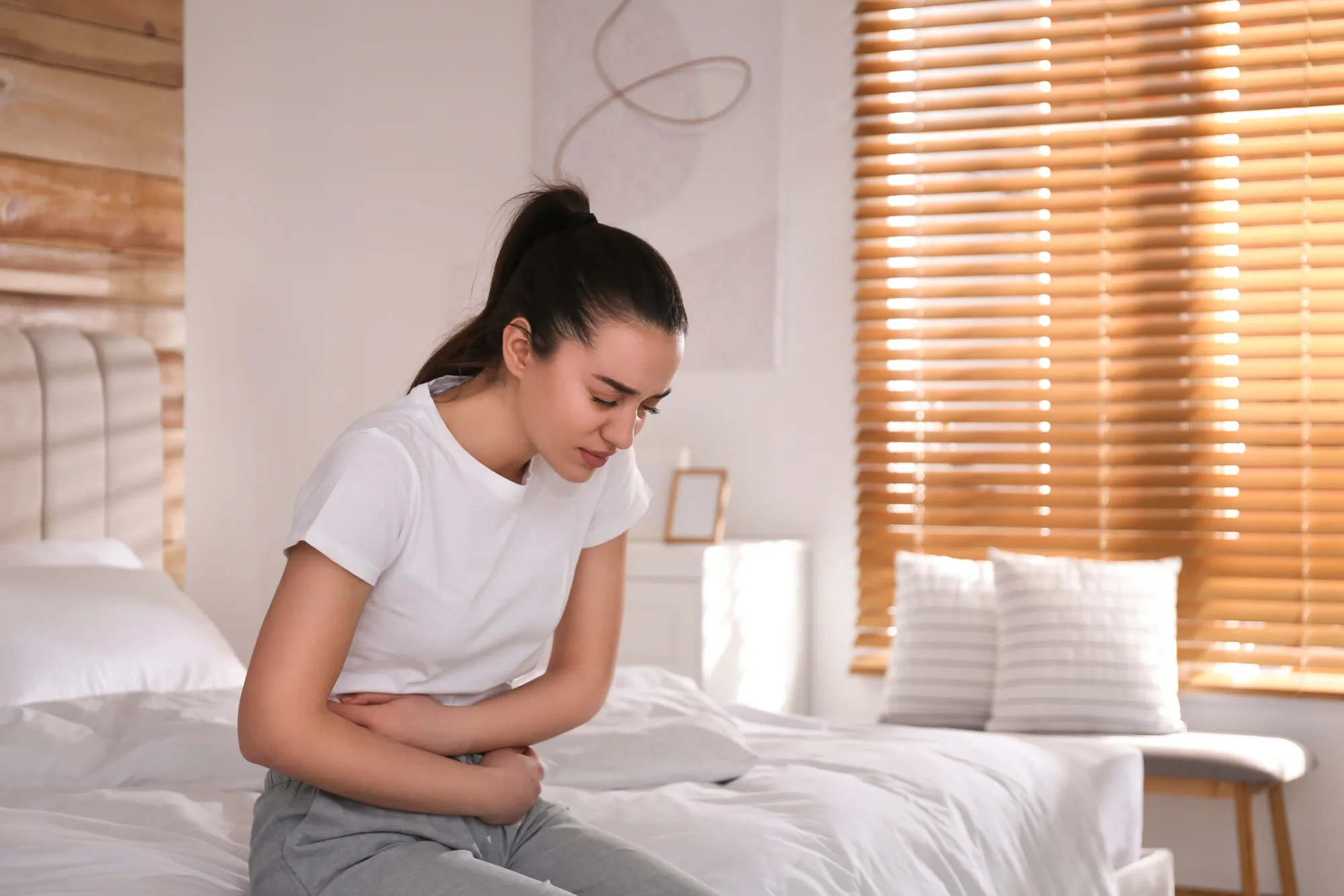 Young woman suffering from stomach pain on bed at home.