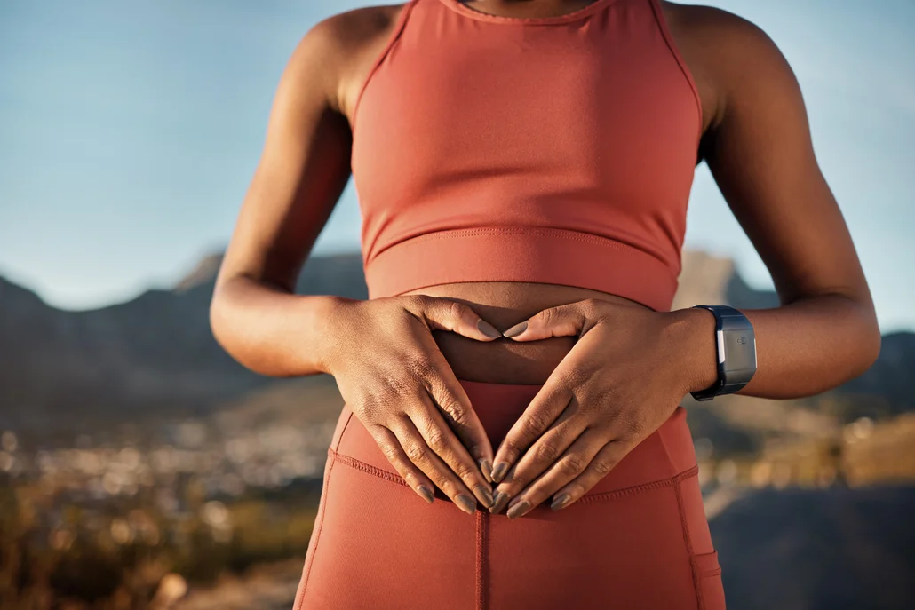A woman outside makeing a heart with her hands over her gut