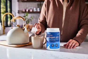 A woman in a scoop of NativePath Collagen PM into a mug with a tea kettle in the background.