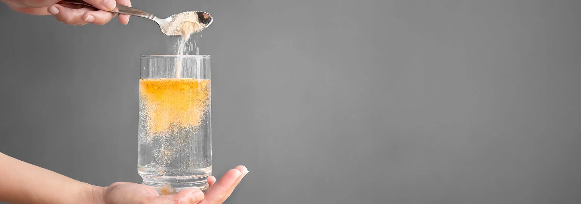 A hand pouring a scoop of an orange fiber supplement into a glass of water