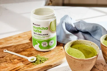 A container of NativePath Matcha Latte on a wooden board next to a mug