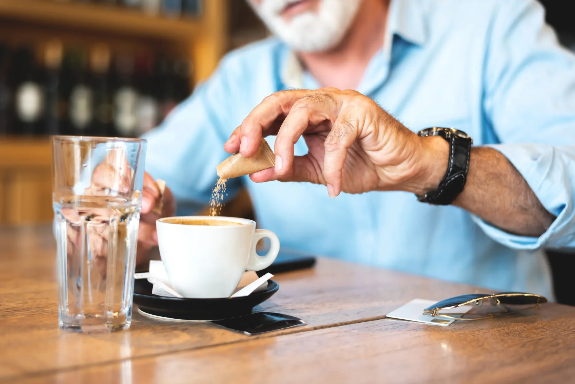 Senior man pouring sugar into his coffee at a restaurant.