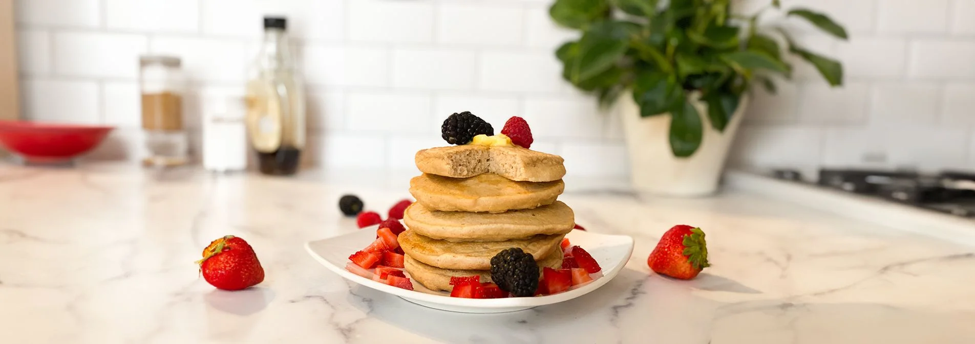 A front shot of a stack of pancakes on a plate topped with berries and a pat of butter.