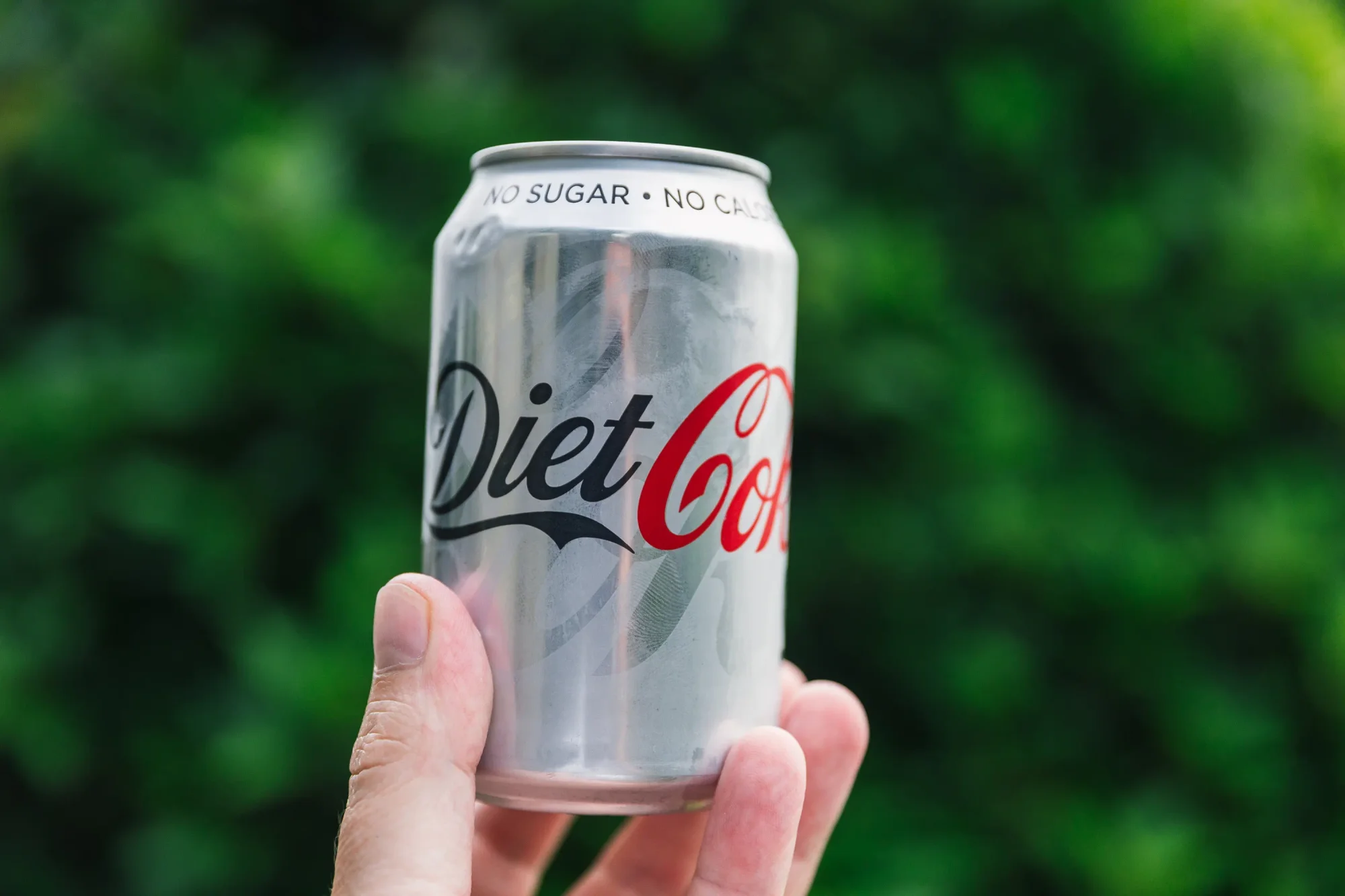 Can of Diet Coke held against green garden background.