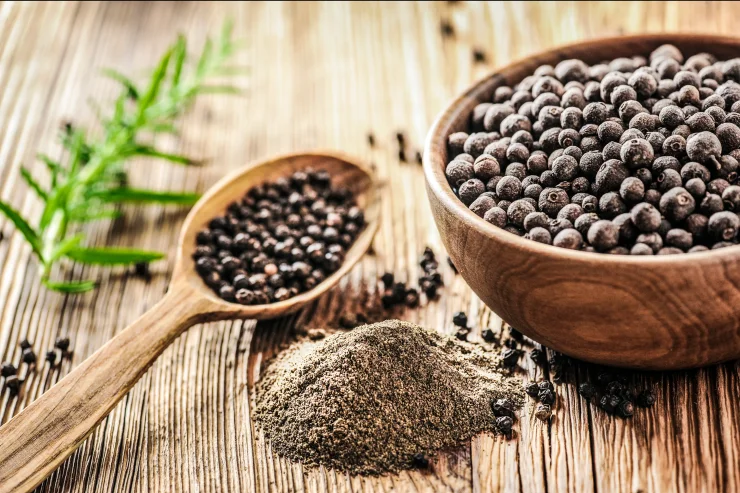 Black peppercorns in wooden bowl on table. Pile of ground black pepper.