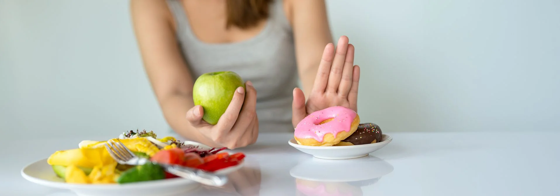 A woman holding an apple and pushing away a plate of donuts