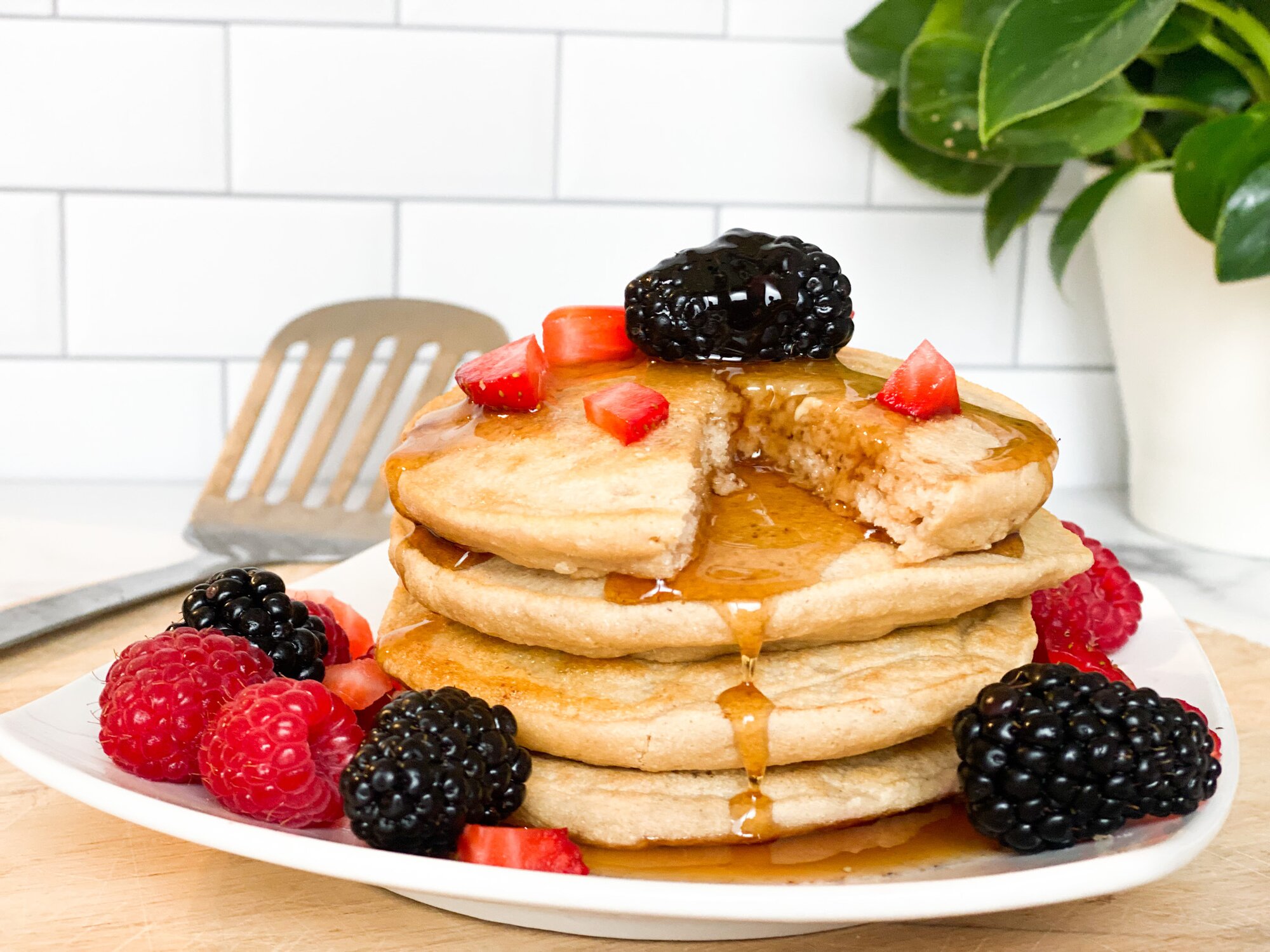 A front view of a plate of pancakes topped with berries and maple syrup with a piece cut out from it