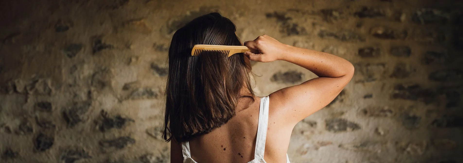 Woman with her back turned running a comb through her straight brown hair.