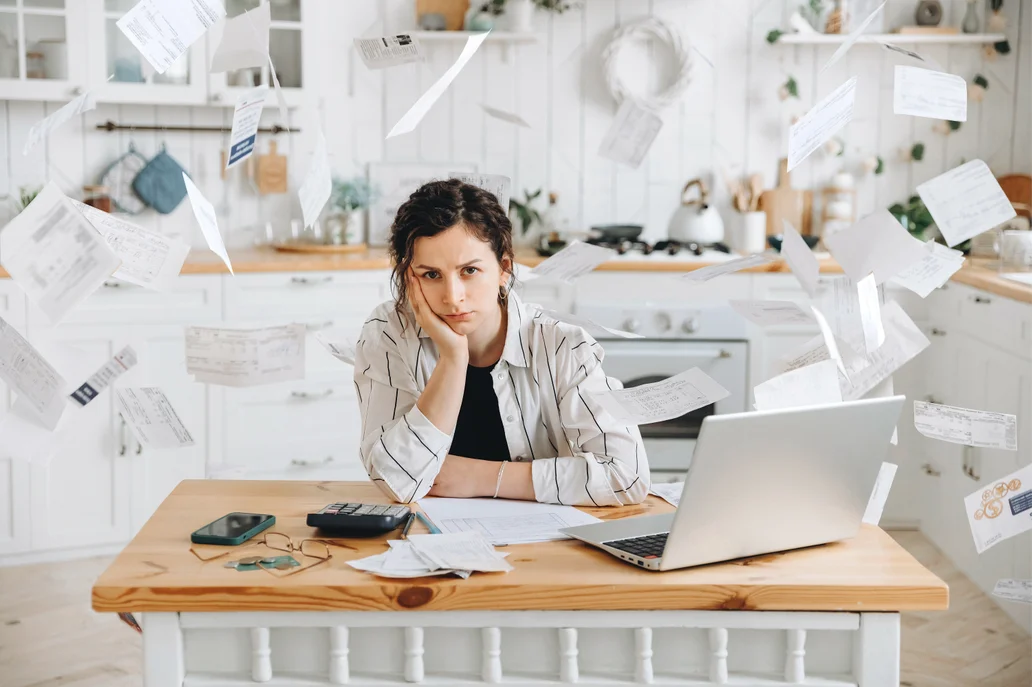 A stressed woman surrounded by paper and her computer.