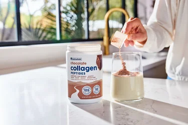 A woman pouring a scoop of NativePath Chocolate Collagen into a glass of almond milk
