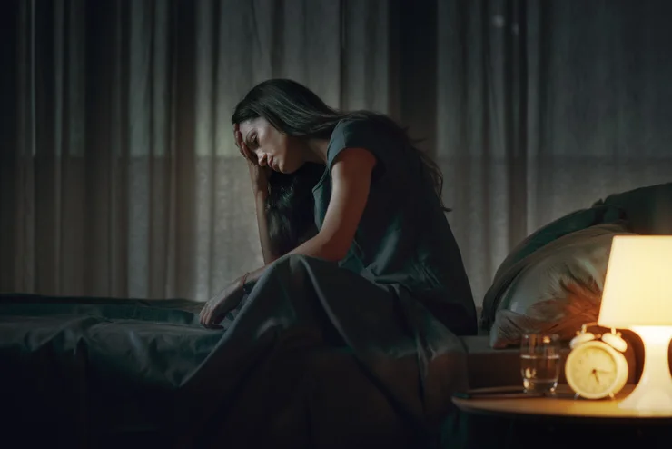 A depressed and anxious woman sitting up in bed, struggling to sleep. 