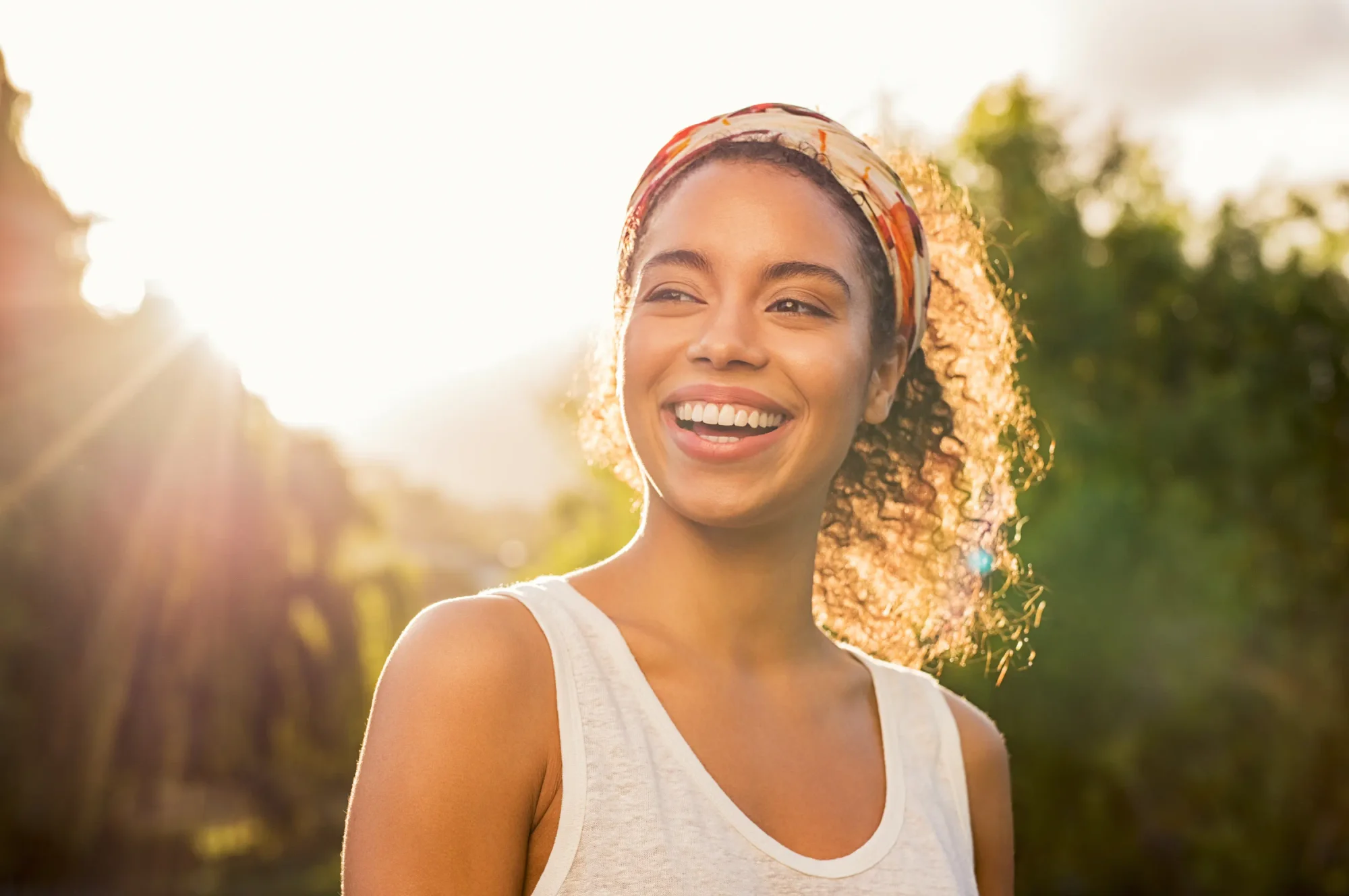 Portrait of smiling woman in the sunshine looking away at nature during sunset.
