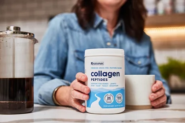 A hand pouring a scoop of NativePath collagen into a coffee mug with a French Press in the background