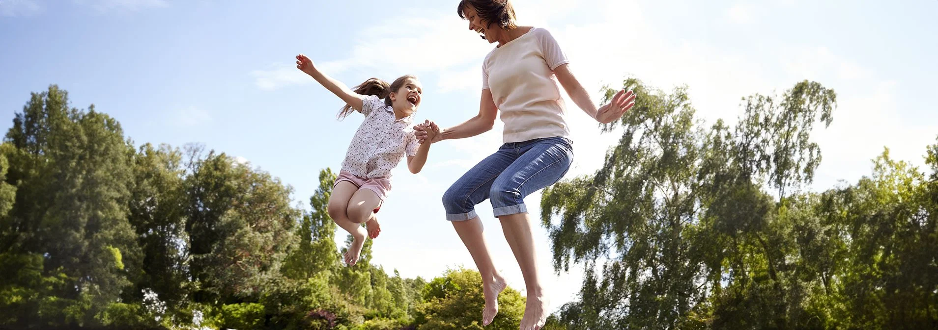 An older woman and a little girl jumping on a trampoline outside.