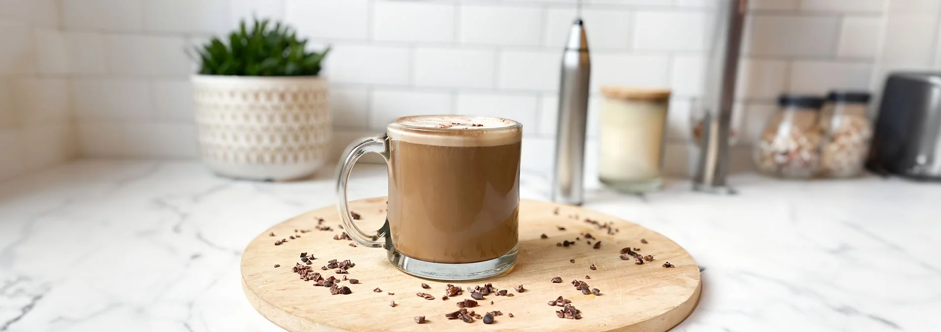 Front view of Mocha MCT Latte in a glass mug on a circular wooden board with a NativePath frother in the background.