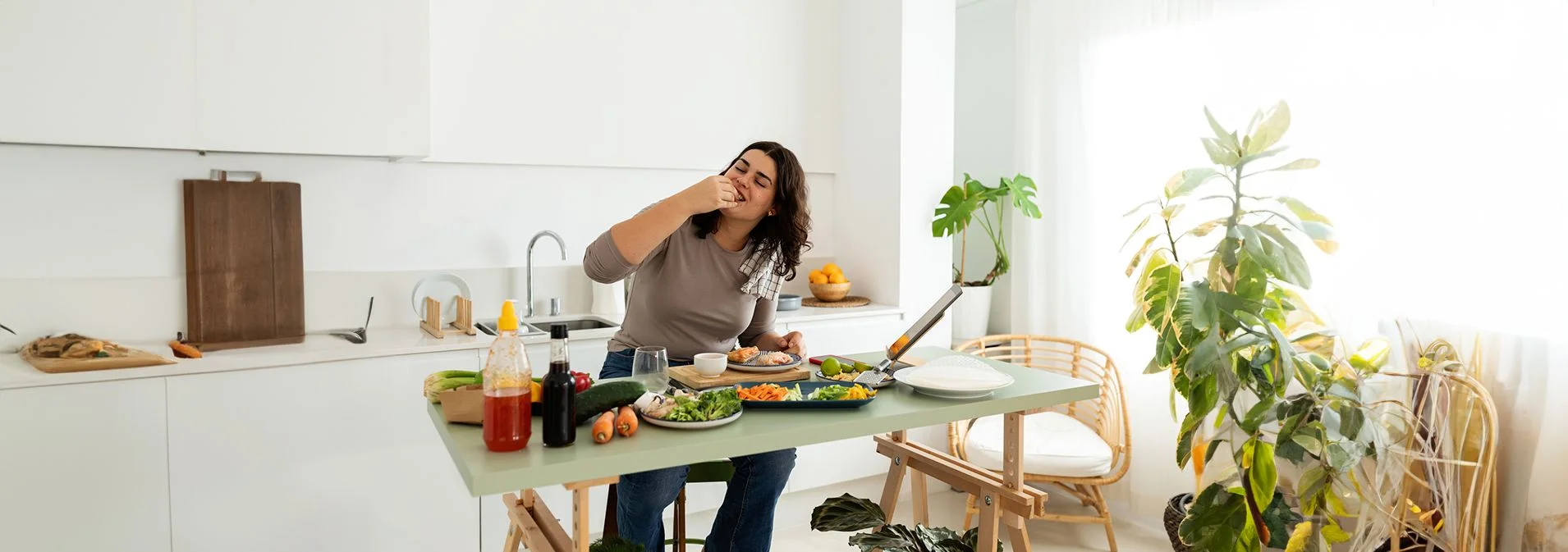 A woman sitting at a table in a kitchen eating fresh veggies 