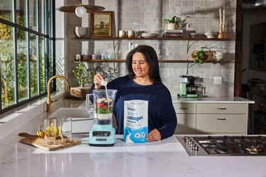 A woman pouring a scoop of NativePath collagen peptides into a mug