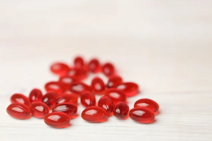 Red krill oil softgels set on a white wooden background.