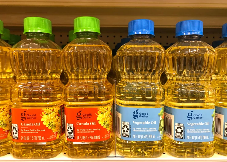 Bottles of canola oil and vegetable oil sitting on grocery store shelves.