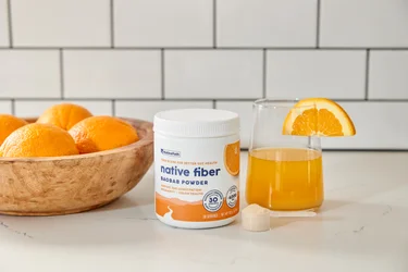 A container and glass of NativePath Native Fiber with a bowl of oranges in the background