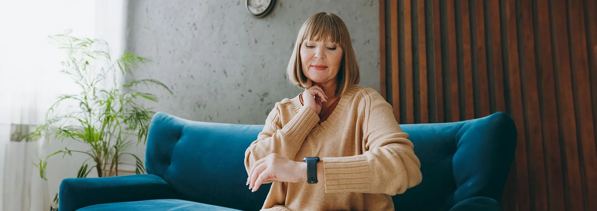 A older woman checking her pulse and heart rate while sitting on a teal couch