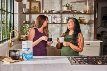 Two women laughing and drinking coffee with NativePath Original Collagen Peptides in the foreground