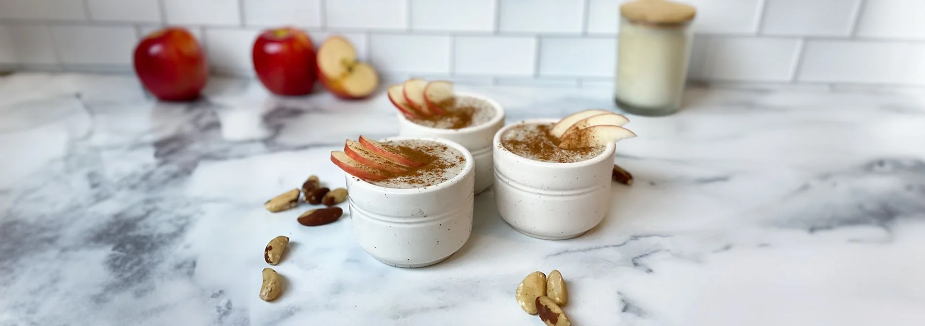 3 ceramic bowls filled with porridge and topped with apple slices. Brazil nuts and apples in the background.