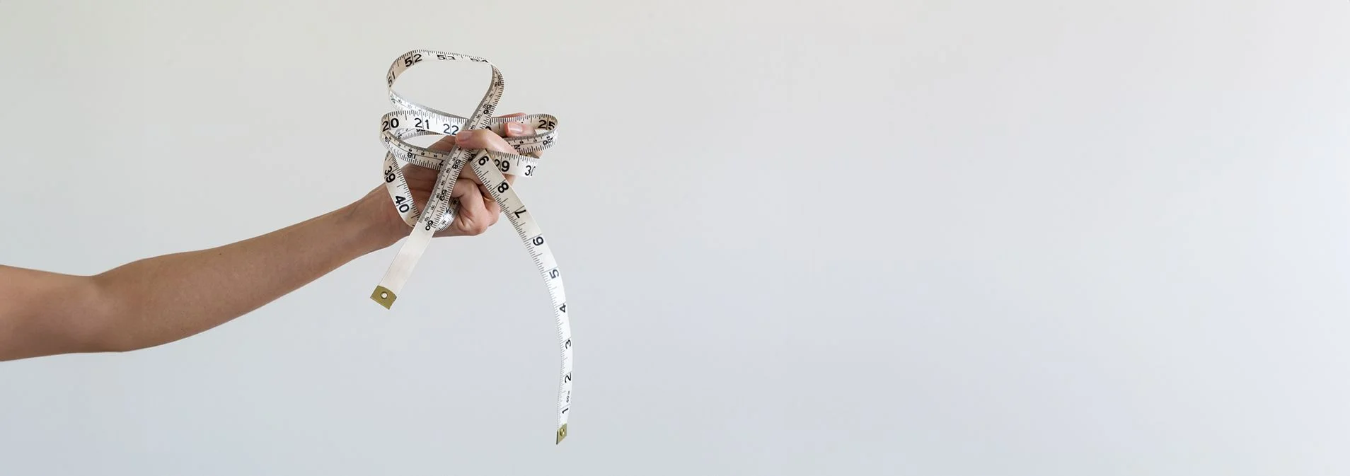 A woman's hand holding a crumpled measuring tape with a white background