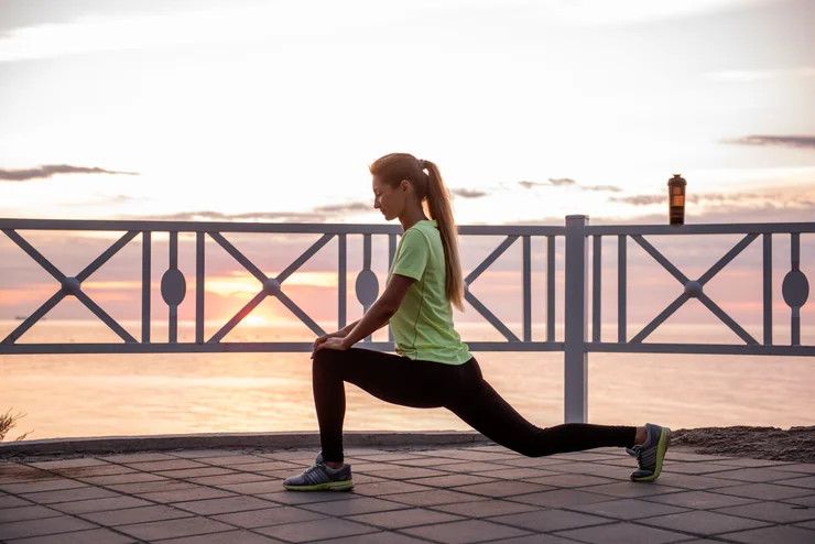 A woman doing yoga outside with the sunset behind her.