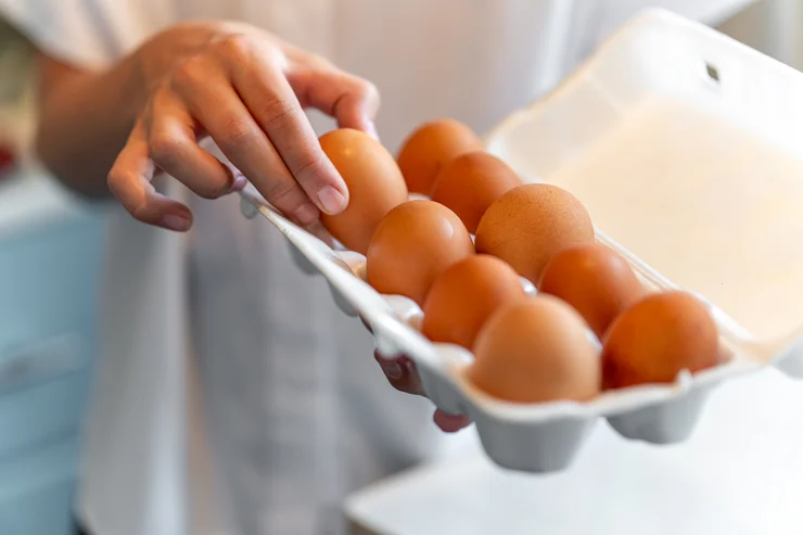 A close up of a person holding a carton of eggs and grabbing one.